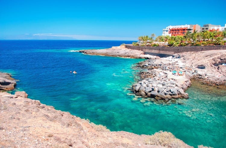 Aerial view of Playa Paraiso featuring crystal-clear turquoise waters, rocky shores, and sunbathers enjoying the beach.