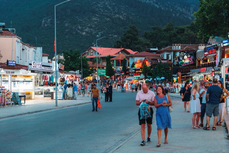 A bustling street in Hisaronu filled with shops, restaurants, and crowds enjoying a lively evening atmosphere.